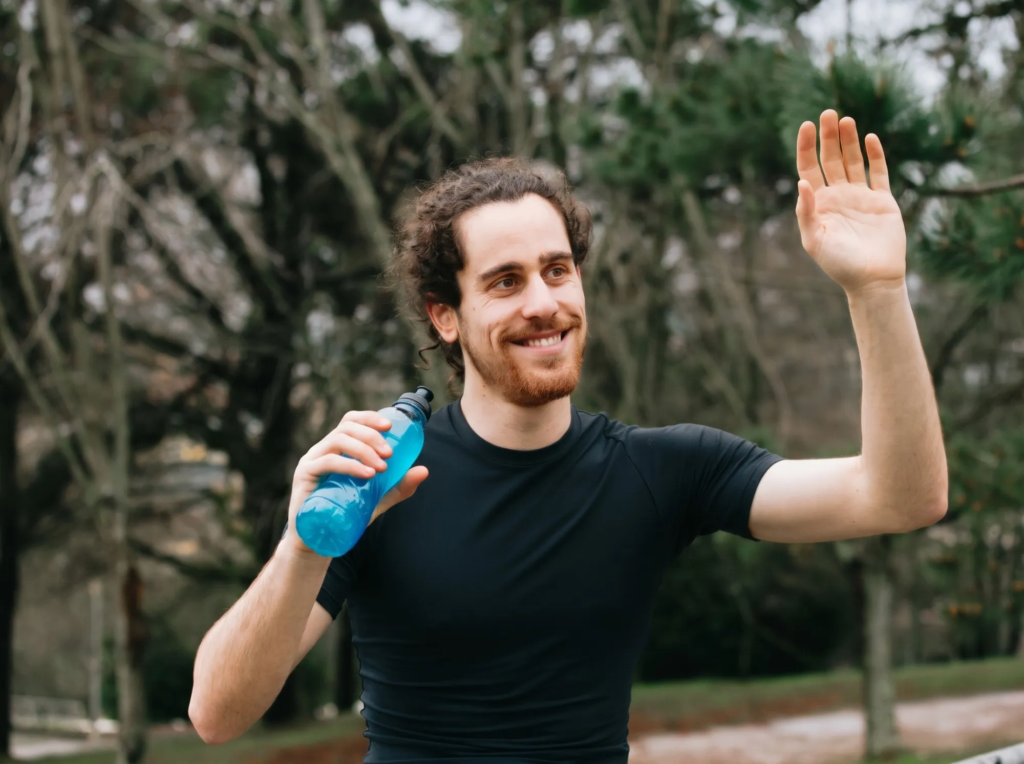 Hombre sonriente saludando al aire libre con una botella de agua