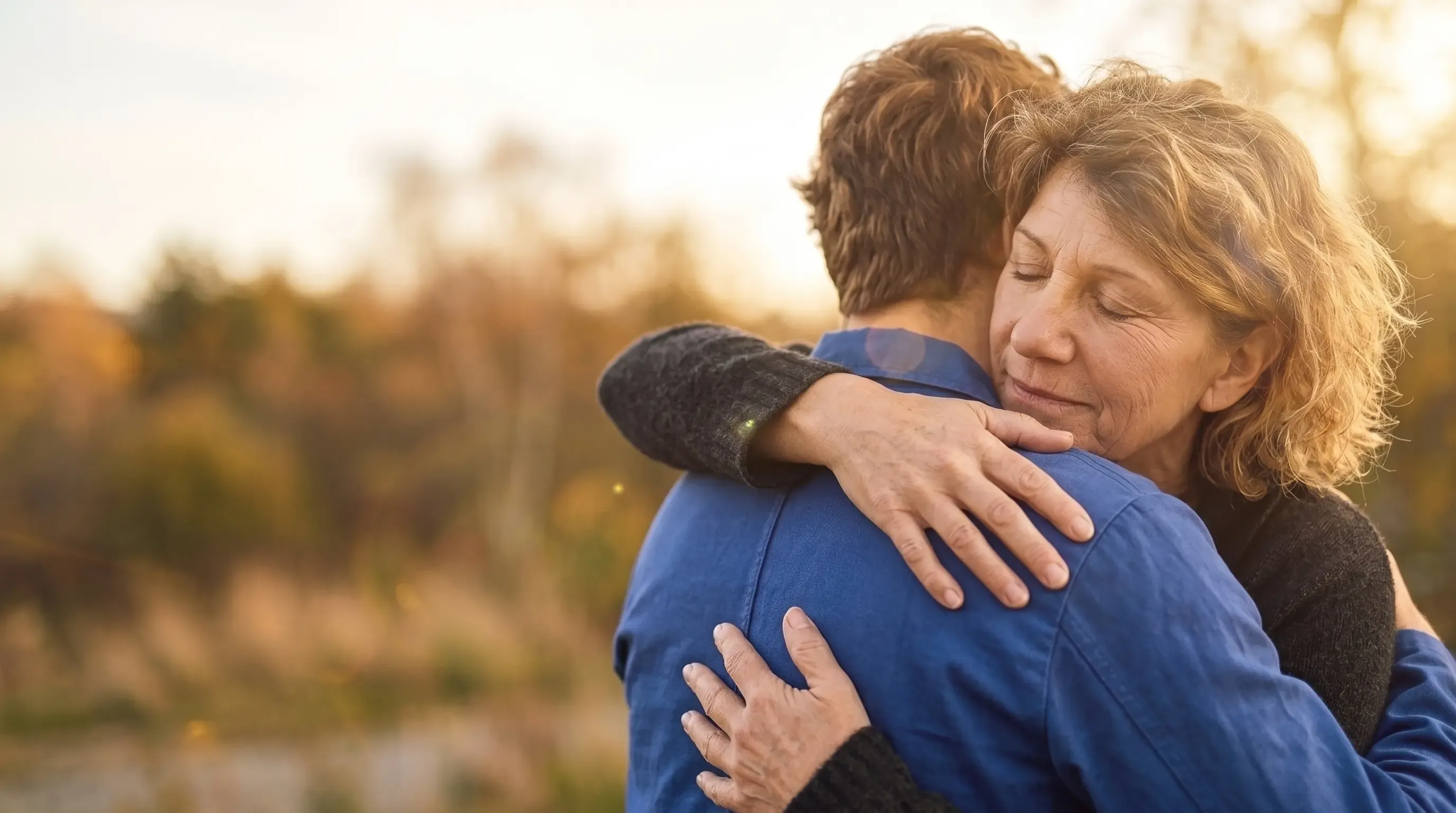 Una madre abraza a su hijo al atardecer con los ojos cerrados